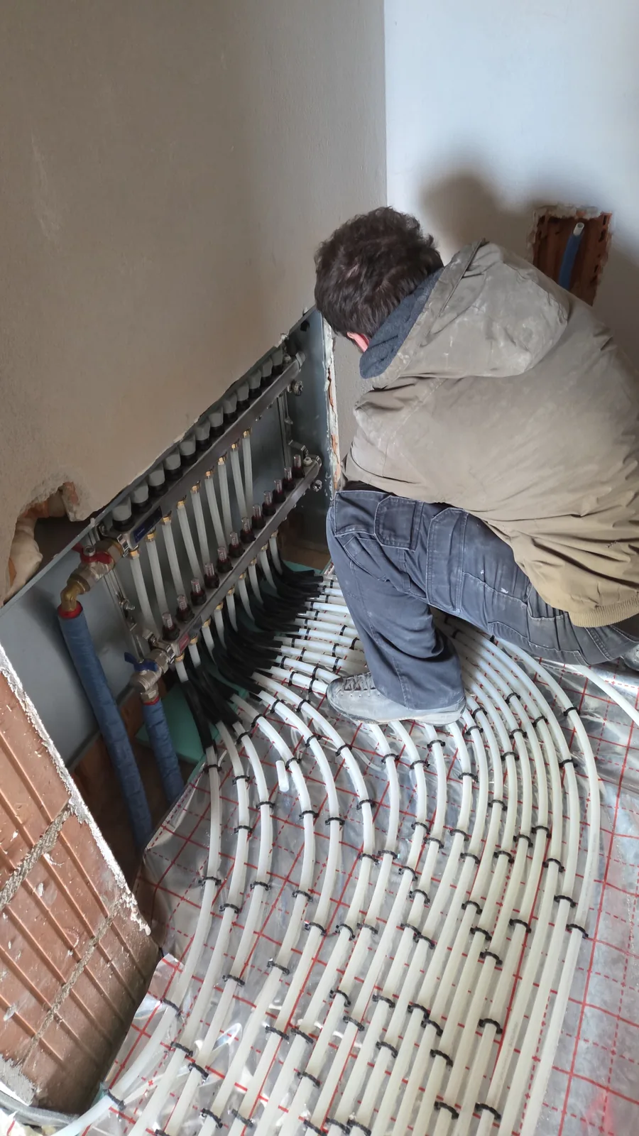 Instalator lucrând la distribuitorul unei încălziri în pardoseală